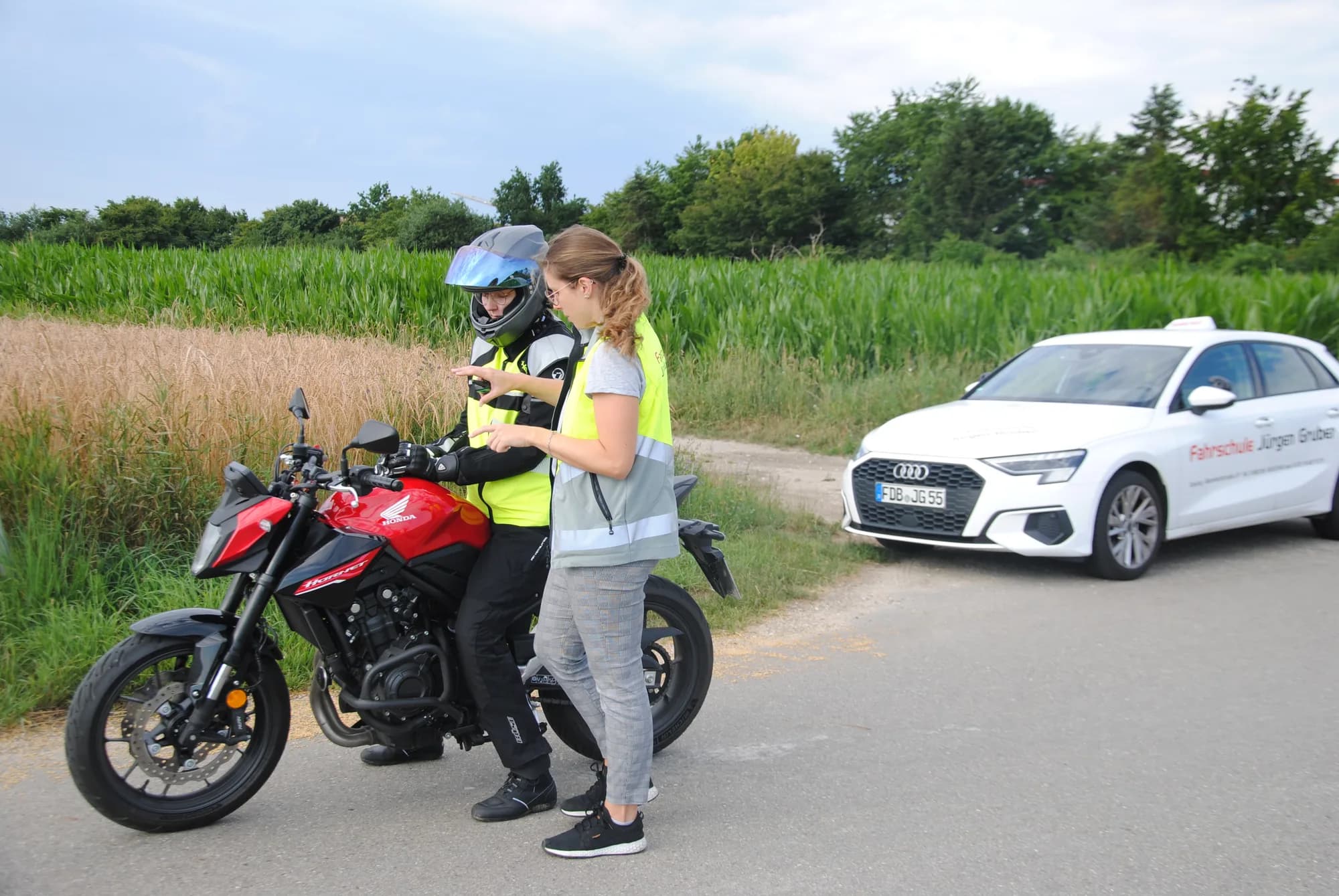 Fahrlehrer auf dem Schulungsmotorrad, dahinter das Fahrschulauto