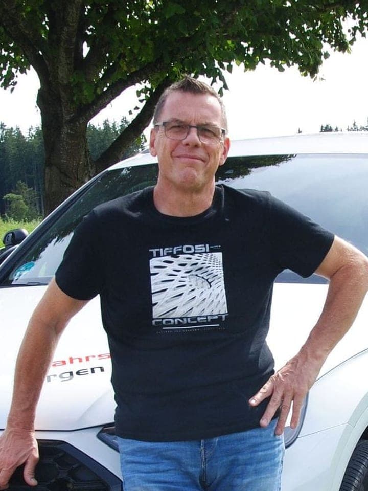 Jürgen Gruber lehnt am weißen Fahrschulwagen mit Aufschrift „Fahrschule Jürgen Gruber, Dasing, Bahnhofstraße 17“