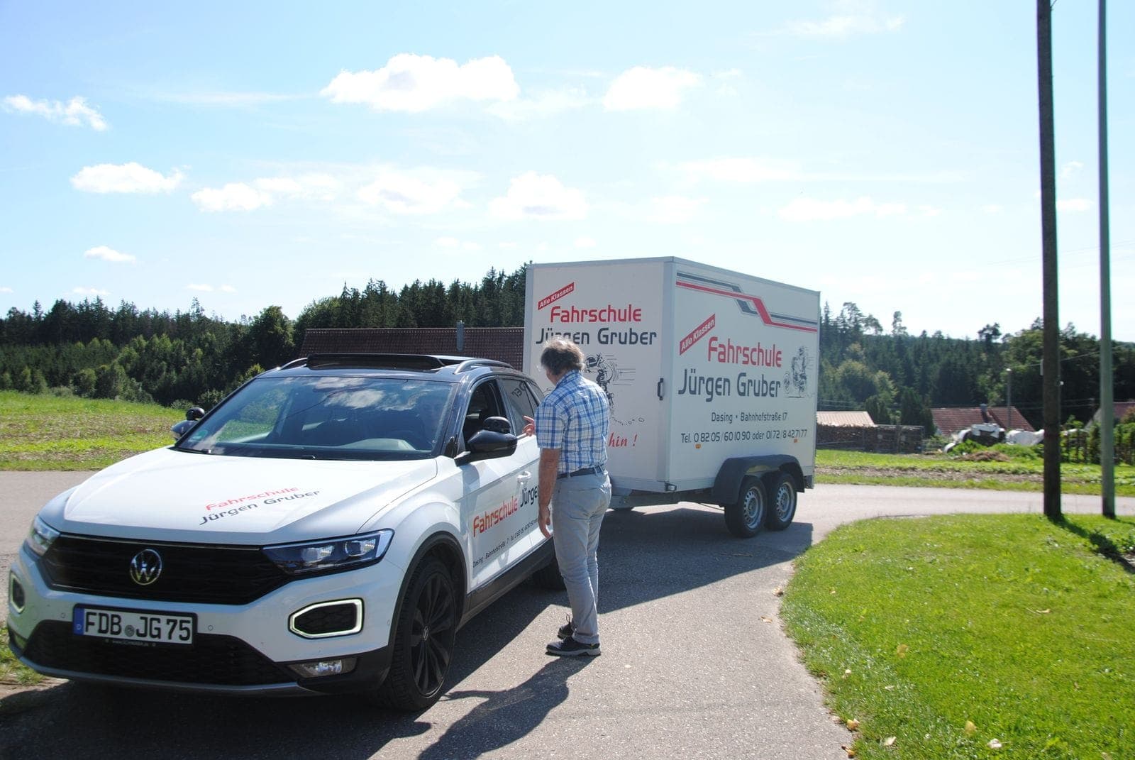 Fahrschul-SUV mit Anhänger auf der Straße vor Wald und Feldern